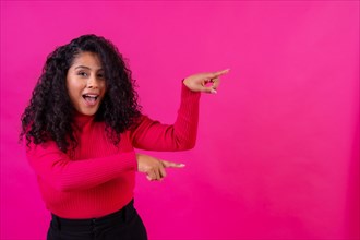 Curly-haired woman pointing to the right on a pink background