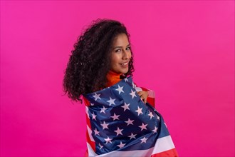 Curly-haired woman embracing usa flag on a pink background
