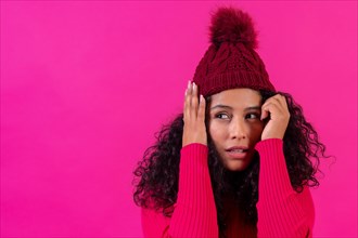 Curly-haired woman in a wool cap on a pink background scared