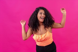 Curly-haired woman in summer clothes on a pink background dancing