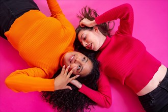 Two multi-ethnic women lying in a happy fashion posing on a pink background