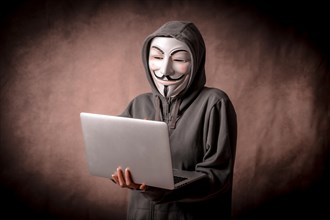 Man with anonymous mask with sweatshirt and with a laptop