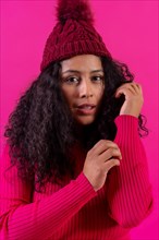 Curly-haired woman in a woolen cap on a pink background portrait with cold