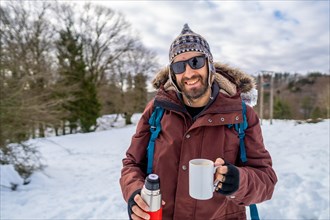 Portrait of man having breakfast a hot coffee from a thermos in winter in the snow