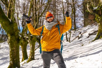 Portrait of a photographer trekking with a backpack taking photos in a beech forest with snow