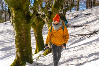 Photographer doing a trekking with a backpack taking pictures of a beech forest with snow