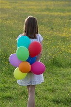 Gilr from behind with colorful balloons in her hands