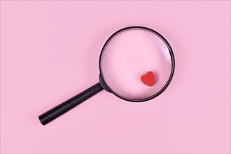 Concept for finding love with magnifier glass and red heart icon on pink background