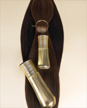 A strand of natural dark hair for extensions with a bottle of care product