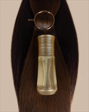 A strand of natural dark hair for extensions with a bottle of care product