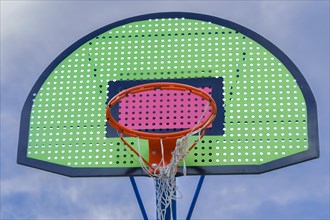 Colorful basketball basket with broken net and blue sky background with clouds
