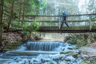 Male hiker walking on bridge over a fairy tale creek