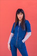 Posing of a smiling brunette girl leaning against a wall in a blue denim outfit