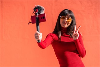 Brunette girl making the victory sign recording a video blog with the mobile