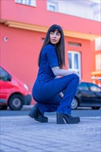 Posing of a brunette model crouching down the street in a denim outfit