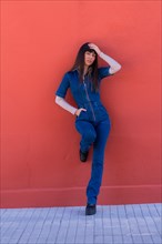 Posing of a smiling brunette girl leaning against a wall in a blue denim outfit