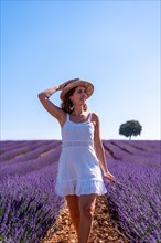 Lifestyle of a woman smiling in a summer lavender field wearing a white dress with a hat