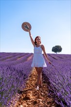 A woman in a summer lavender field in a white dress enjoying nature
