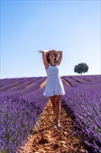 A woman in a summer lavender field in a white dress enjoying nature