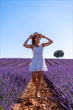 Lifestyle of a woman smiling in a summer lavender field wearing a white dress with a hat