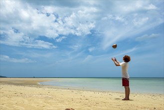 Young man throws a coconut in the air on the beach