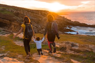 Lgbt couple of women with a child walking in the sunset on the coast by the sea