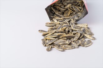 Roasted sunflower seeds with salt coming out of their bag on white background and copy space