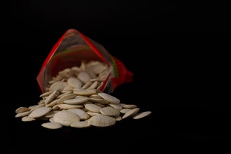 Roasted pumpkin seeds with salt coming out of their red bag on a black table with copy space