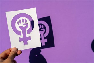 A woman holding the symbol of the fight for feminism on a purple background