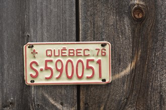 Vintage 1976 Quebec province license plate displayed on side wall of wood plank storage shed