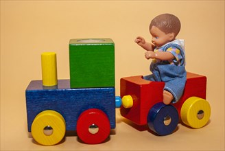 A little doll boy sits on a toy train made of wood
