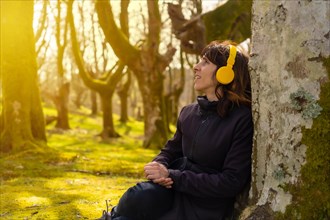 A girl listening to music with yellow headphones in the forest at sunset