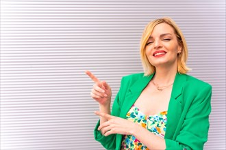 Portrait of a pretty blonde model in a green jacket pointing to the left
