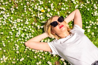 A young blonde girl in a hat and sunglasses breathing pure haire in the spring in a park in the city