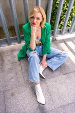 A blonde model woman in a green jacket sitting on the floor in a building in the city