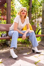 Blonde tourist girl on summer vacation sitting on a bench in a park