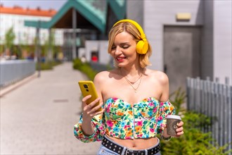 Pretty blonde woman listening to music in the city with yellow headphones and the phone