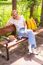 Portrait of a blonde tourist girl on summer vacation sitting on a bench in a park