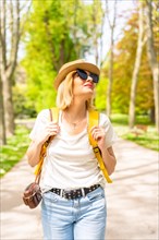 A tourist blonde woman with a hat and sunglasses walking in the spring in a park in the city