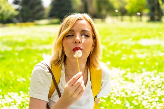 A smiling blonde woman blowing on the dandelion plant