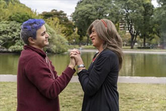Transgender woman and her gay son holding hands and lovingly looking at each other in a park