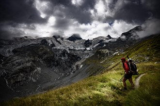 Mountaineer in front of Bernina group with Rosegg glacier and dramatic clouds at blue hour