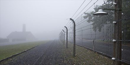 Reconstructed camp fence with crematorium in the fog at beech forest concentration camp