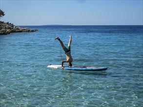 Man doing headstand on a SUP in crystal clear water