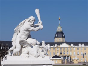 White sculpture of a man with a club and a dragon and in the background Karlsruhe Castle
