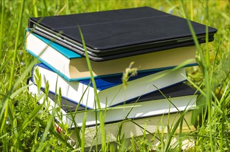 Pile of various books and tablet in the fresh green grass