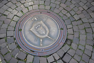Round manhole cover with city coat of arms and paving stones