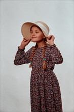 Portrait of a girl holding her sun hat tightly against a white background