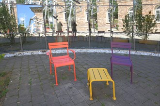 Three colourful chairs in front of the glass wall and window segments reflection