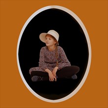 Girl in dress with pigtails and hat sits on the ground. With oval frame and text freedom